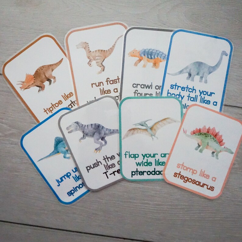 Puede incluir: Un conjunto de 8 tarjetas de memoria coloridas que representan diferentes dinosaurios con instrucciones sobre c&oacute;mo moverse como ellos. Las instrucciones incluyen "caminar de puntillas como un Triceratops", "correr r&aacute;pido como un Velociraptor", "arrastrarse en cuatro patas como un Ankylosaurus", "estirar el cuerpo alto como un Brachiosaurus", "saltar como un Spinosaurus", "empujar el mundo como un T-Rex", "batir las alas como un Pterodactyl", y "pisotear como un Stegosaurus".