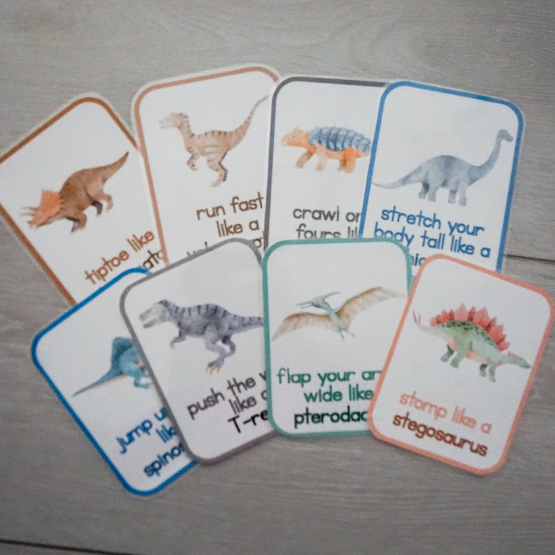 Puede incluir: Un conjunto de 10 tarjetas ilustradas coloridas que representan diferentes dinosaurios con instrucciones sobre c&oacute;mo moverse como ellos. Las tarjetas incluyen instrucciones como "caminar de puntillas como un Triceratops", "correr r&aacute;pido como un Velociraptor", "arrastrarse en cuatro patas como un Ankylosaurus", "estirar el cuerpo como un Brachiosaurus", "empujar el suelo como un T-Rex", "batir las alas como un Pterodactyl", y "pisotear como un Stegosaurus".