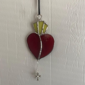May include: A stained glass heart ornament with a yellow crown and a silver cross hanging from it.