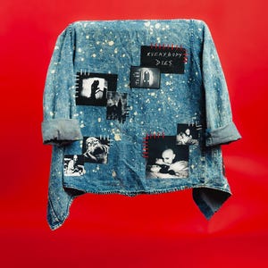 May include: A blue acid-wash denim jacket featuring white paint splatters and multiple black and white rectangular patches. The patches display various dark imagery and the text "EVERYBODY DIES" stitched with red thread onto the fabric.