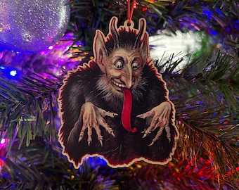 Puede incluir: Un adorno navideño de estilo vintage que representa a un diablo de piel roja con cuernos, una larga lengua roja y garras afiladas. El adorno está hecho de madera y tiene un aspecto desgastado y antiguo.
