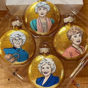 Könnte beinhalten: Set aus vier goldenen Weihnachtskugeln mit Glitzer, die Porträts der Golden Girls zeigen. Jede Kugel zeigt eine andere Golden Girl in einem farbenfrohen Outfit.