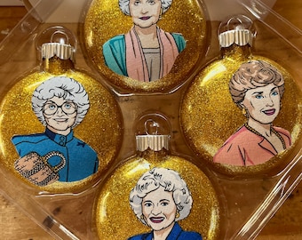 Könnte beinhalten: Set aus vier goldenen Weihnachtskugeln mit Glitzer, die Porträts der Golden Girls zeigen. Jede Kugel zeigt eine andere Golden Girl in einem farbenfrohen Outfit.