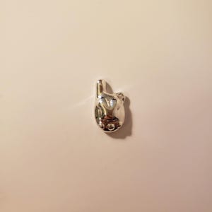 May include: A small, silver-colored charm in the shape of a hand, with the index finger and thumb extended. The charm has a smooth, reflective surface and is likely made of metal. The design is detailed, with visible finger and thumb shapes.