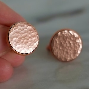 Puede incluir: Un par de pendientes redondos de cobre con textura martillada.