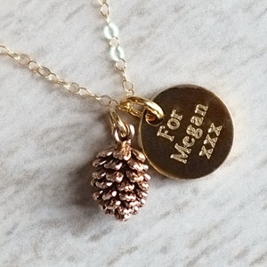 Può includere: Collana d'oro con un ciondolo a forma di pigna e un'etichetta rotonda in oro che dice "Per Megan xxx".