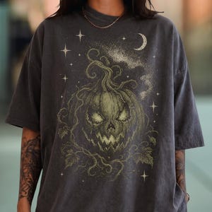 May include: A charcoal gray short-sleeve t-shirt featuring a large, detailed graphic of a glowing, vine-covered jack-o'-lantern. The design includes a crescent moon, scattered stars, and swirling vines in shades of pale green and off-white.