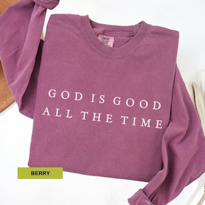 May include: Berry-colored long-sleeve shirt with the text "GOD IS GOOD ALL THE TIME" in white. The shirt is made of a soft material and has a crew neck. The word "BERRY" is in a green rectangle.