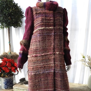 May include: A long, textured coat in shades of burgundy, brown, and cream. The coat features a high collar and sleeves in a contrasting deep burgundy knit. The overall design is a mix of woven and knit textures, creating a unique and warm aesthetic.