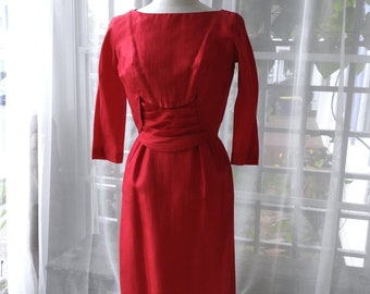 May include: A red dress with a fitted bodice and a slightly flared skirt. The dress has a bateau neckline and three-quarter sleeves.