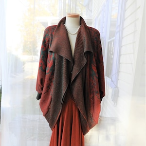 May include: A long, red and green patterned cardigan with a draped collar. The cardigan is worn over a rust-colored skirt.