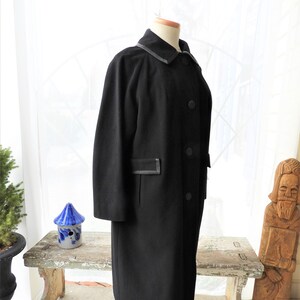 May include: A black long-sleeved coat with a collar and button closure. The coat has a black trim around the collar and pockets.