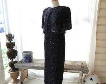 May include: A black sequined dress with a matching jacket. The dress has a long, flowing skirt and a fitted bodice. The jacket has short sleeves and a round neckline. The dress is on a mannequin in a room with a window and a wooden bench.