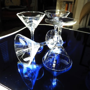 Peut inclure: Quatre verres à martini en verre transparent avec des motifs gravés reposent sur une surface bleu foncé. Les verres sont vides et réfléchissent la lumière.