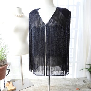 May include: A black beaded cardigan with a V-neckline and long sleeves. The cardigan is made of a sheer fabric and has a beaded fringe at the hem.