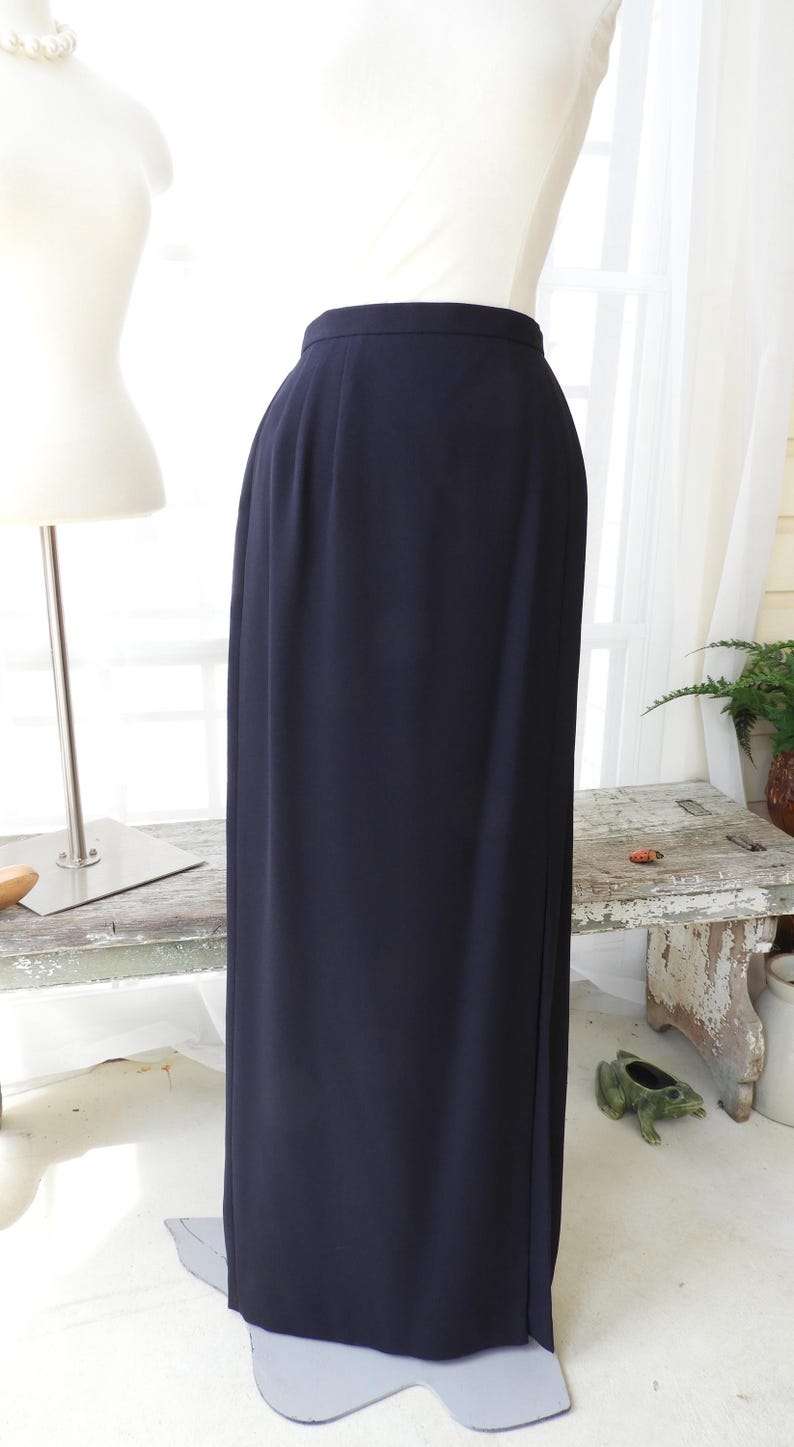 May include: A long, dark blue skirt with a straight silhouette. The skirt is made of a smooth, wrinkle-resistant fabric.