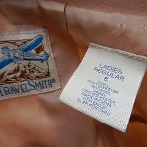 May include: A white tag with black text that reads "LADIES REGULAR 8 SHELL 55% POLYESTER 45% WOOL LINING: 100% POLYESTER MADE IN CHINA STYLE#4230 OVER FOR CARE" attached to a peach-colored fabric.
