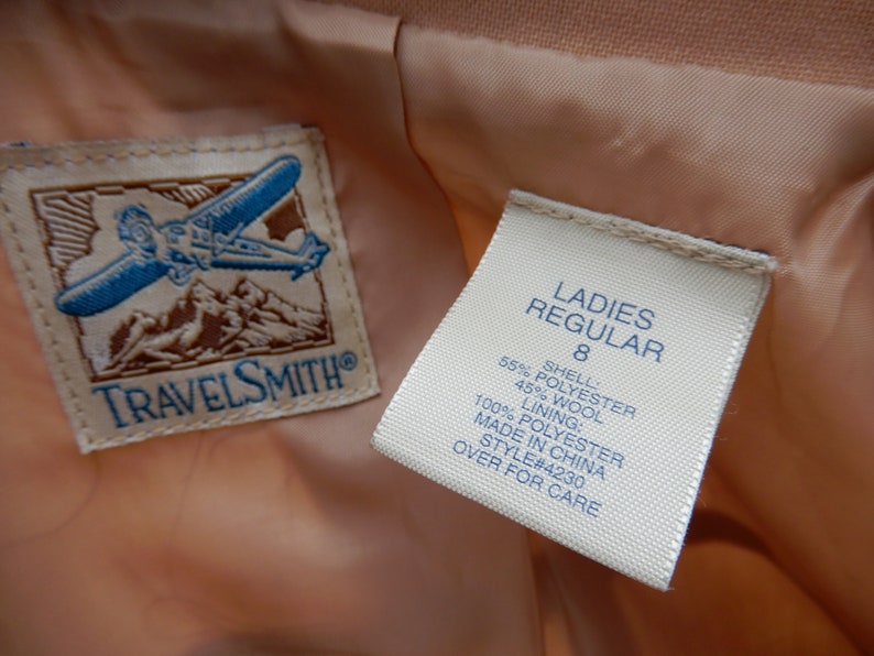 May include: A white tag with black text that reads "LADIES REGULAR 8 SHELL 55% POLYESTER 45% WOOL LINING: 100% POLYESTER MADE IN CHINA STYLE#4230 OVER FOR CARE" attached to a peach-colored fabric.