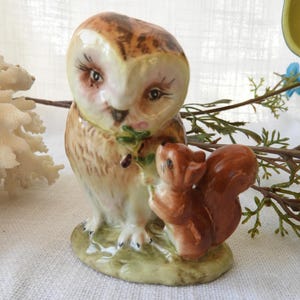 May include: A ceramic figurine of an owl and squirrel. The owl has brown and cream-colored feathers, with detailed facial features. The squirrel is brown and stands beside the owl. The base is green with grass.