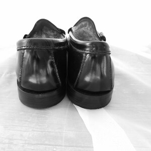 May include: A pair of black leather loafers with a suede lining. The loafers are shown from the back, with the heels facing the camera.