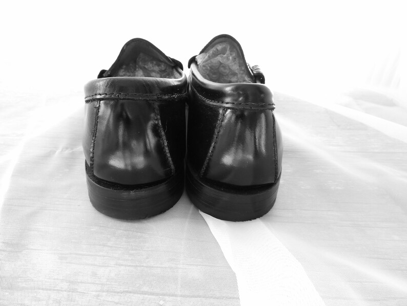 May include: A pair of black leather loafers with a suede lining. The loafers are shown from the back, with the heels facing the camera.