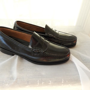 May include: A pair of black leather loafers with a penny strap detail. The loafers have a slightly rounded toe and a low heel.