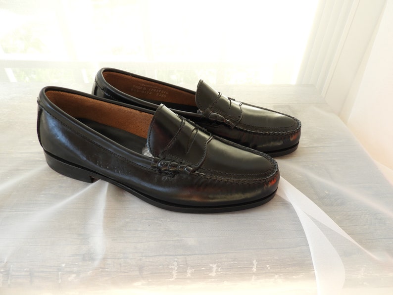 May include: A pair of black leather loafers with a penny strap detail. The loafers have a slightly rounded toe and a low heel.