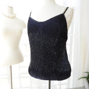 May include: A black beaded sleeveless top with a scoop neck. The top is made of small, dark blue beads that are sewn together in a vertical pattern.