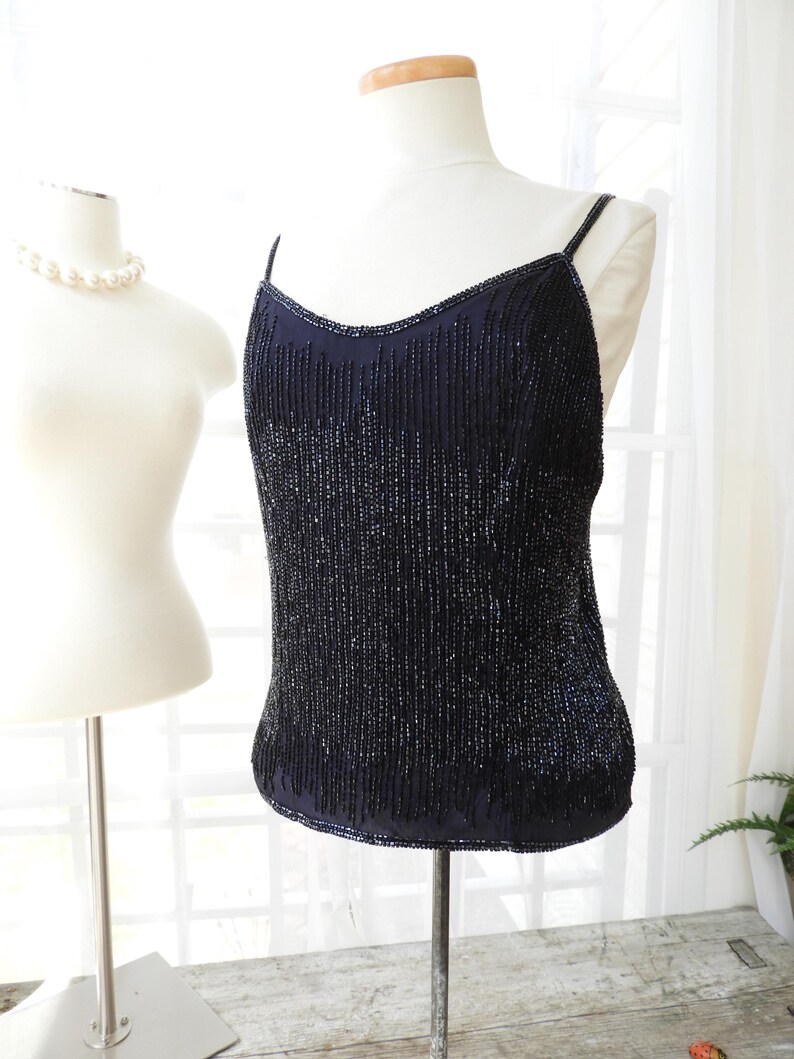 May include: A black beaded sleeveless top with a scoop neck. The top is made of small, dark blue beads that are sewn together in a vertical pattern.
