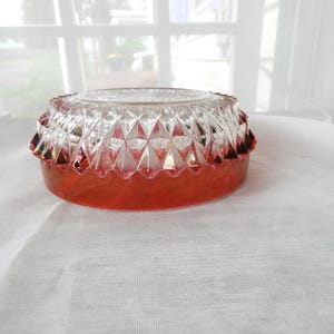 May include: A vintage, clear glass ashtray with a ruby red base. The ashtray features a diamond-cut pattern on the upper portion and a scalloped edge. The base is a solid, vibrant red. The ashtray is a decorative item.
