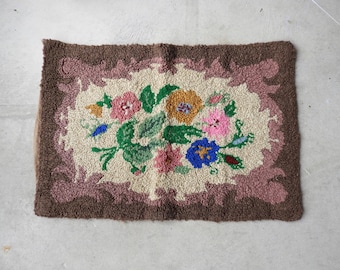 Puede incluir: Una alfombra rectangular con un diseño floral. La alfombra presenta una disposición central de flores coloridas en rosa, azul, amarillo y naranja, rodeadas de hojas verdes. El borde es marrón y rosa.