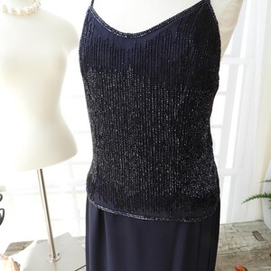 May include: A black beaded sleeveless dress with a fitted bodice and a flowing skirt. The bodice is covered in small black beads that create a shimmering effect.