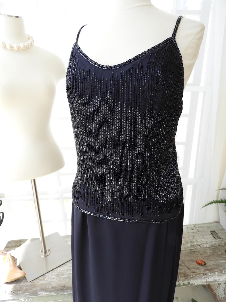 May include: A black beaded sleeveless dress with a fitted bodice and a flowing skirt. The bodice is covered in small black beads that create a shimmering effect.