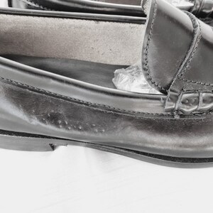 May include: A pair of black leather loafers with a stitched detail around the toe and a decorative strap across the vamp.
