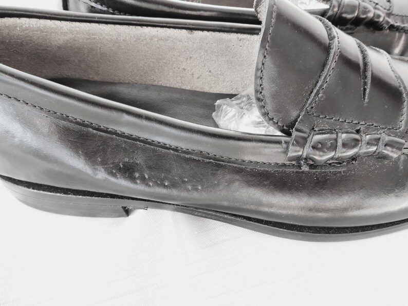 May include: A pair of black leather loafers with a stitched detail around the toe and a decorative strap across the vamp.