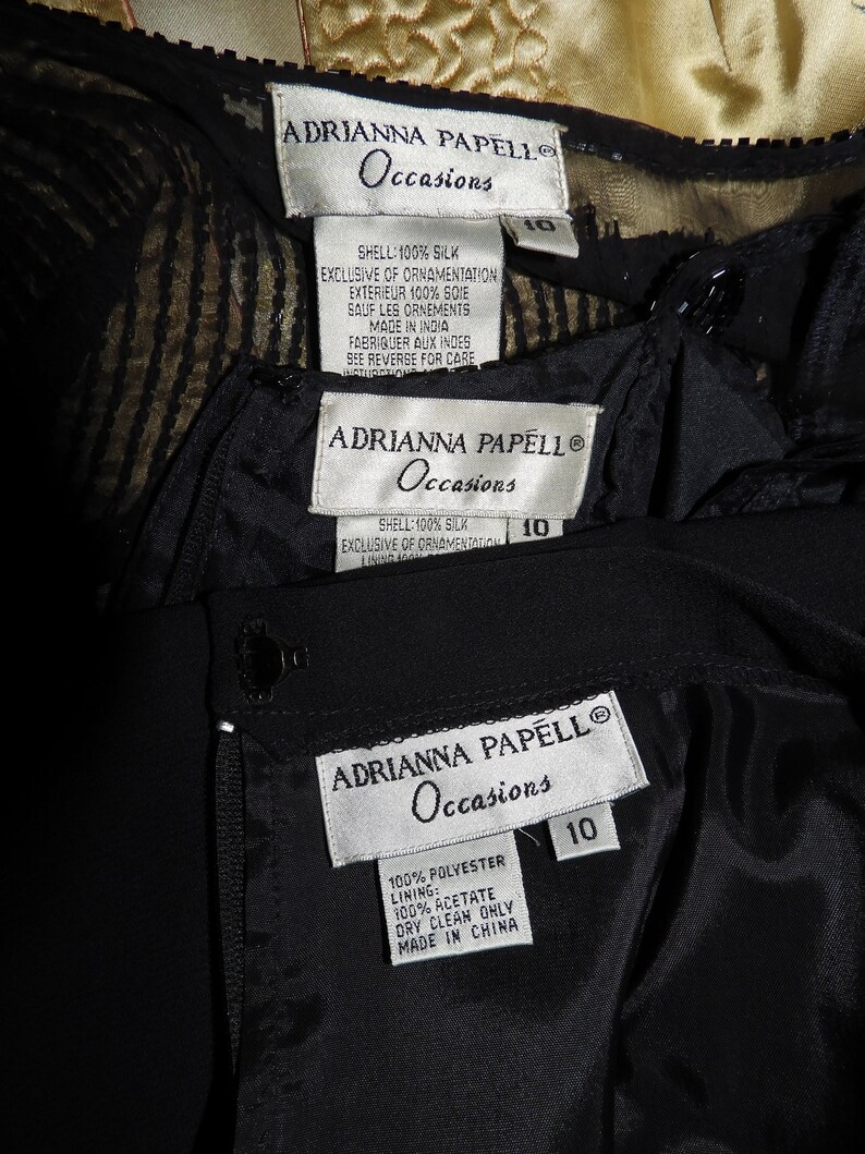 May include: Three black and white clothing labels with the text "ADRIANNA PAPELL Occasions" and size 10. The first label is for a silk dress, the second label is for a silk dress, and the third label is for a polyester dress.