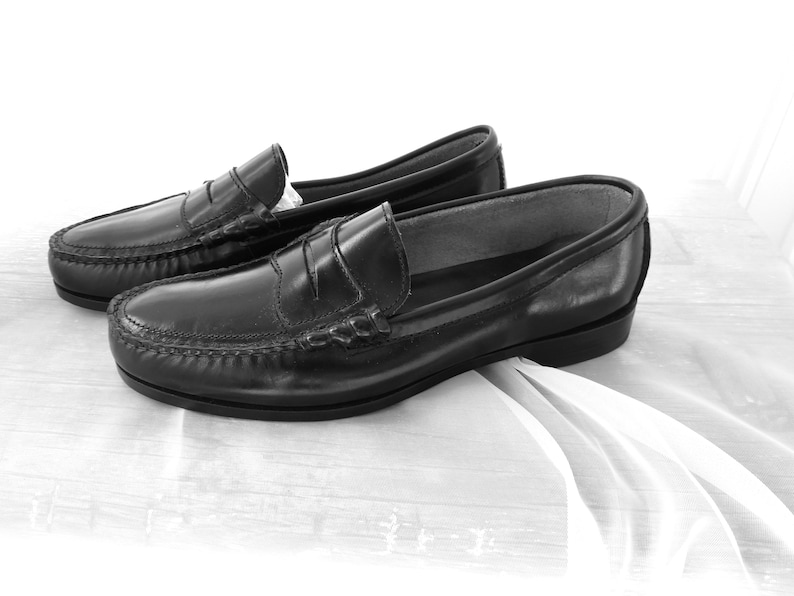May include: A pair of black leather loafers with a penny strap detail. The loafers are on a white fabric surface.
