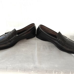 May include: A pair of black leather loafers with a tassel detail. The loafers have a penny strap and a leather sole.