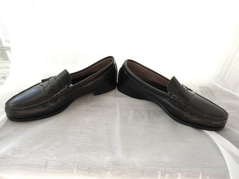 May include: A pair of black leather loafers with a tassel detail. The loafers have a penny strap and a leather sole.