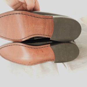 May include: Close-up of the bottom of a pair of black leather shoes. The shoes have a leather sole with the text "Leather Sole Made in USA" printed on the insole.