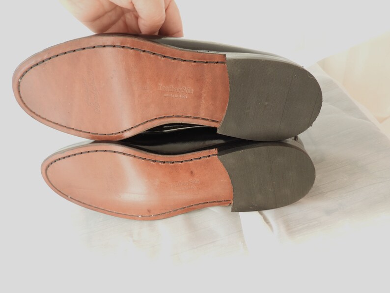 May include: Close-up of the bottom of a pair of black leather shoes. The shoes have a leather sole with the text "Leather Sole Made in USA" printed on the insole.