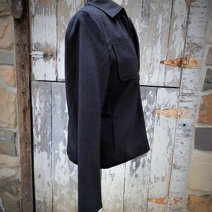May include: A black blazer with a zipper closure and a single pocket on the left side. The blazer is on a white mannequin and has long sleeves.