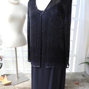 May include: A black beaded jacket with a long black skirt. The jacket has a V-neck and is made of small beads that hang down in a fringe. The skirt is a simple, straight cut.