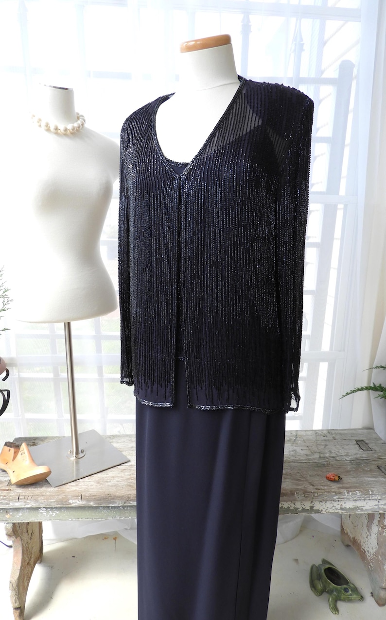May include: A black beaded jacket with a long black skirt. The jacket has a V-neck and is made of small beads that hang down in a fringe. The skirt is a simple, straight cut.