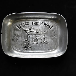 Può includere: Un vassoio in metallo argentato con un design in rilievo di un camino e le parole "Bless This Home".