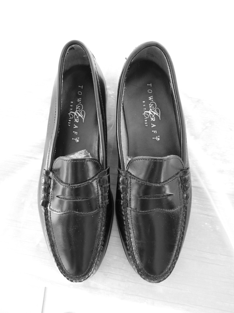 May include: A pair of black leather loafers with a penny strap detail. The loafers have a stitched edge and the brand name "Towncraft" is printed on the inside of each shoe.