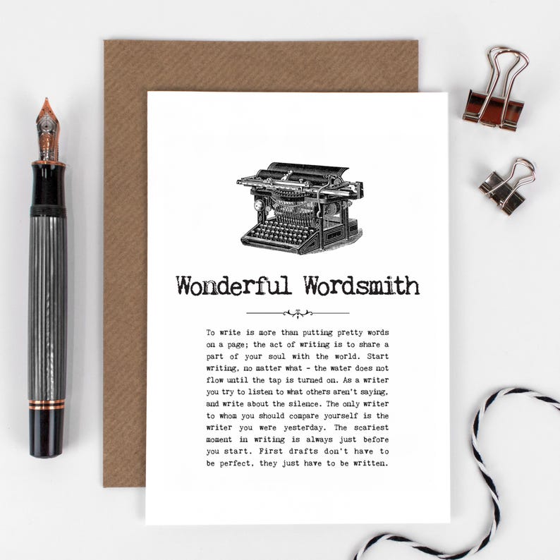 Pu&ograve; includere: Un biglietto di auguri con la scritta "Wonderful Wordsmith" e un'illustrazione di una macchina da scrivere d'epoca. Sono visibili anche una penna stilografica nera e argento e due fermagli argentati.