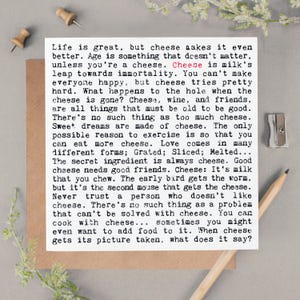 May include: A square white card featuring black typewriter-style text about cheese, with the word Cheese highlighted in red. The card is placed on a brown paper background, accompanied by two wooden push pins, a metal sharpener, and a wooden pencil.