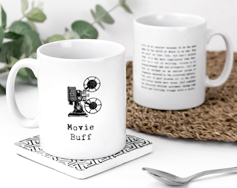 May include: Two white ceramic mugs. The front mug features a black illustration of a vintage film projector above the text "Movie Buff" in a typewriter font. The back mug displays a block of printed text in a similar typewriter style font.