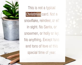 Könnte beinhalten: Eine weiße Grußkarte mit roségoldenem Metallic-Text, der lautet: This is not a typical Christmas card. Not a snowflake, reindeer, or elf in sight. No Santa, or snowmen, or holly or ivy. No anything. Except tons and tons of love at this special time of year.